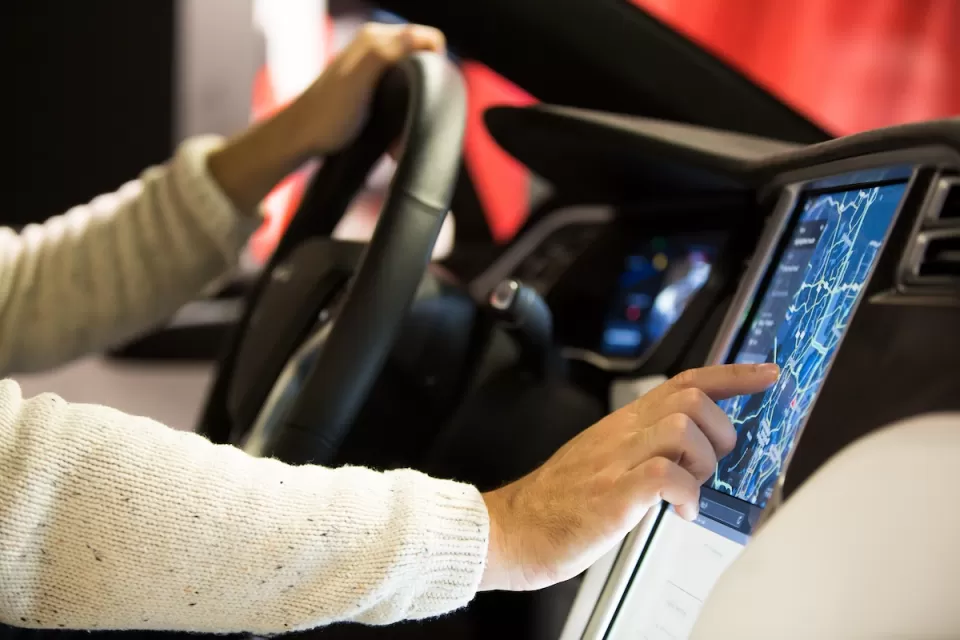Close-up of man's hands on steering wheel and digital screen in Tesla car's driver's seat.
